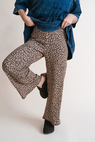 A person wearing leopard-print wide-leg pants with a blue ruffled blouse and dark brown slip-on shoes, shown from the waist down against a plain light background.