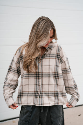Model holding the hem of the boxy khaki plaid button down top to show the relaxed shape