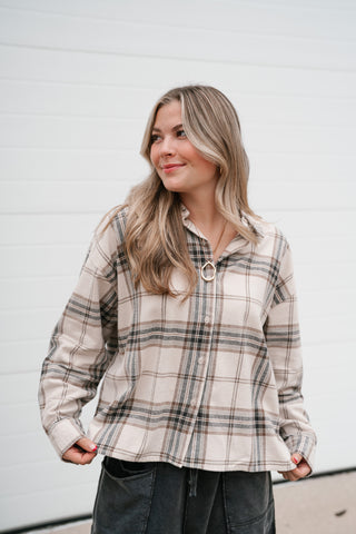 Model looking to the side in the khaki and black plaid collared button up shirt