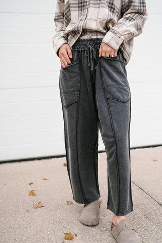Front view of the washed black utility pants with drawstring waist, patch pockets and suede clogs