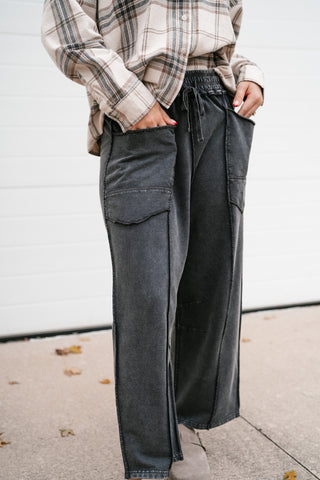 Model with hands in the patch pockets of the black utility barrel leg pants