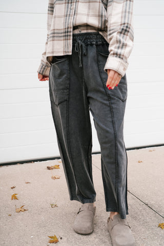 Front view of the washed black drawstring pants showing the cropped length and center seam detail