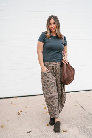 Woman wearing the Free People We The Free Atlas Crew Tee in washed black with printed drawstring pants and a brown tote