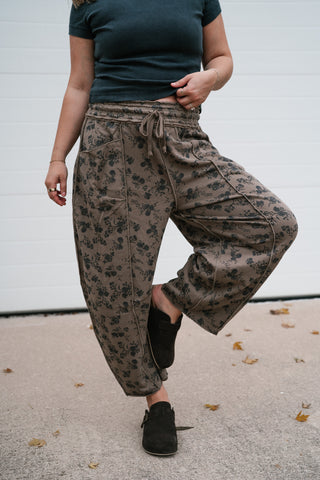 Model lifting one knee to show the roomy fit of the mocha floral barrel pants