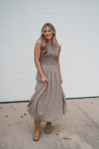 Woman wearing the Elodie brown gingham smocked sleeveless midi dress with tan cowboy boots