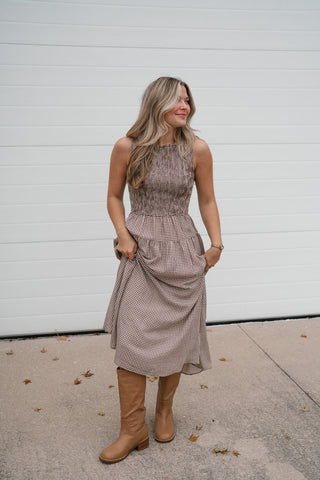 Model holding the skirt of the brown gingham check sleeveless midi dress