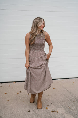 Model with a hand on her hip wearing the brown gingham smocked midi dress and tan boots