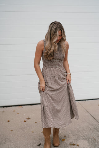 Model looking down in the fitted brown gingham smocked dress with a tiered A-line skirt