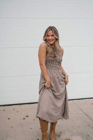 Smiling model holding out the skirt of the brown and white gingham midi dress