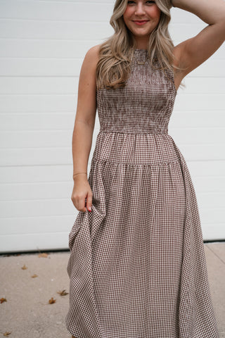 Front view of the brown gingham smocked bodice midi dress with a hand in her hair