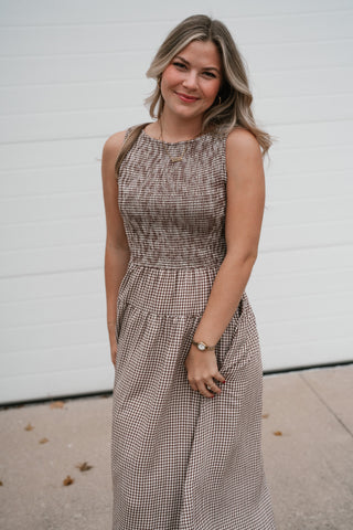 Smiling model in the fitted brown gingham smocked sleeveless dress
