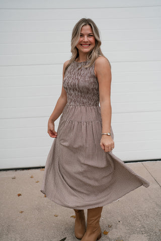 Model twirling the full tiered skirt of the brown gingham midi dress