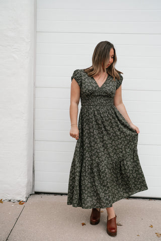 Model holding the skirt of the olive green floral tiered midi dress