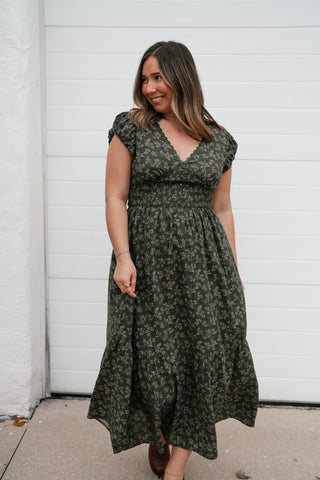Model holding out the skirt of the dark green floral V-neck dress to show the full tiered hem