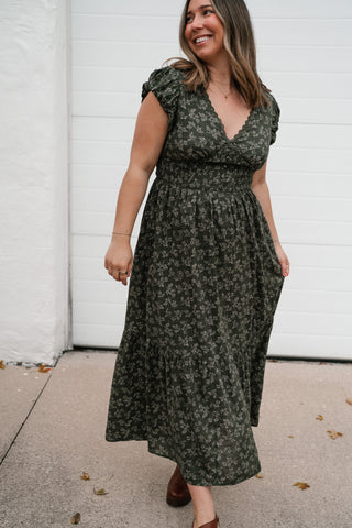 Smiling model walking in the Evergreen Fields olive floral V-neck midi dress