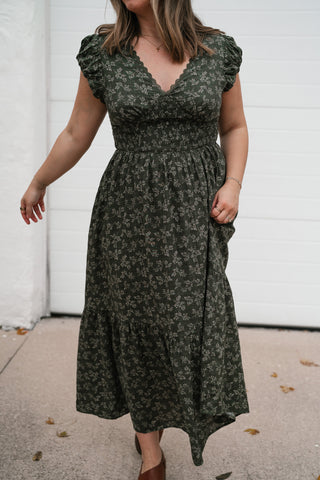 Model twirling the flowy tiered skirt of the olive green floral midi dress
