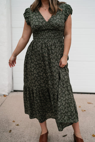 Model walking in the olive floral midi dress showing the smocked waist and flowy tiered skirt