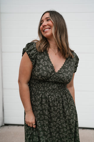 Smiling model in the olive green floral midi dress showing the V-neckline and flutter sleeves