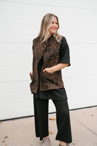 Model with hands in the front pockets of the brown leopard print vest styled with an all-black outfit