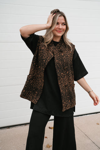 Model with a hand in her hair wearing the relaxed brown leopard print puffer vest