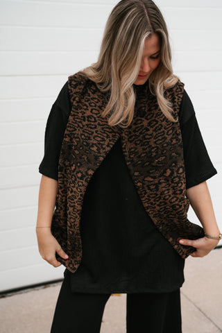 Waist-up view of the leopard print vest held open to show the overlapping front and relaxed shape