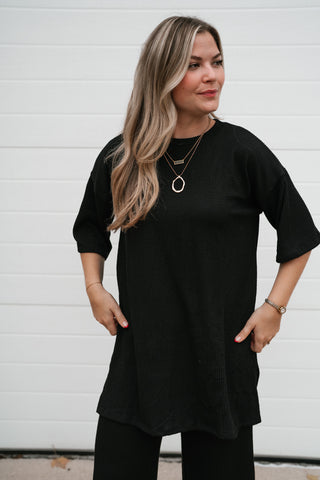 Waist-up view of the oversized black ribbed top showing the boat neckline and relaxed drape