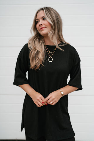 Front view of the oversized black ribbed top showing the boat neckline and long length