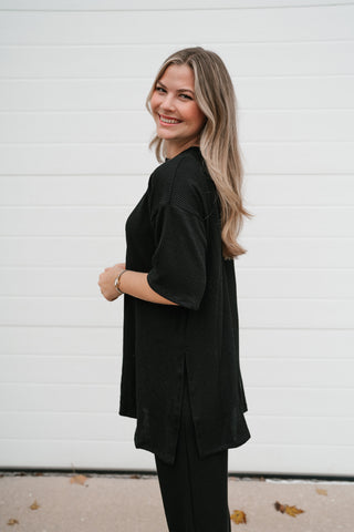 Side view of the black ribbed oversized top showing the side slit and relaxed fit