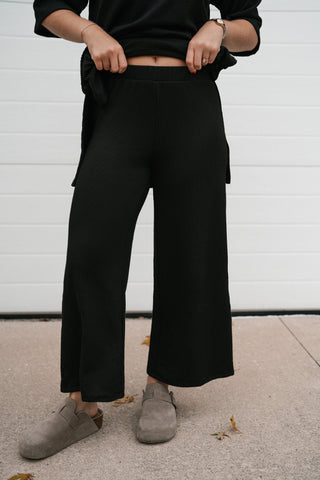 Front view of the black ribbed set pants with wide cropped leg and the matching top