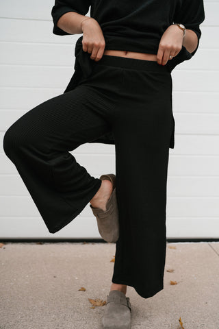 Model lifting one knee to show the stretch and wide leg of the black ribbed lounge pants