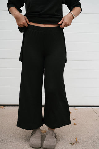 Model holding the waistband of the high waisted black ribbed wide leg pants