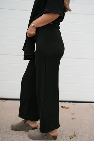 Side view of the black ribbed wide leg pants showing the relaxed fit and cropped length