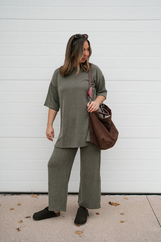 Woman wearing the Everyday Olive ribbed set top with the matching wide leg pants and a brown tote