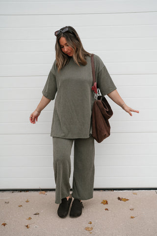 Model with arms out showing the relaxed boxy fit of the olive ribbed set top