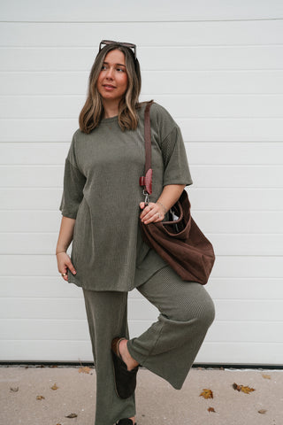 Model lifting one knee in the olive ribbed matching set with a brown shoulder bag