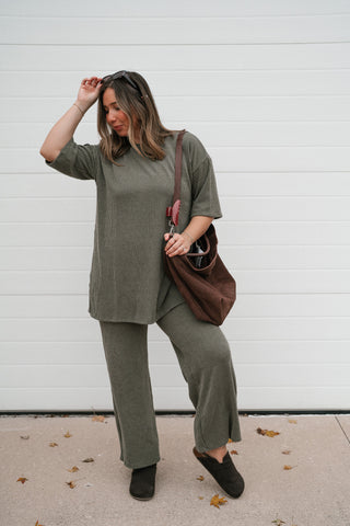 Model with a hand in her hair wearing the olive green ribbed lounge set