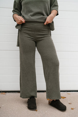 A person wearing ribbed olive green wide-leg pants and a matching top, standing outdoors in front of a white garage door.