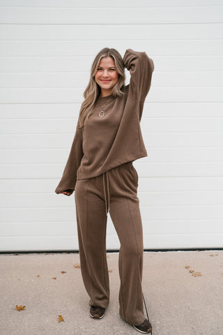 Model raising one arm to show the wide long sleeve of the mocha ribbed crewneck top