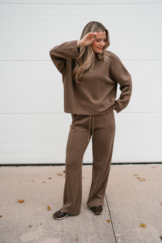 Model wearing the mocha ribbed crewneck top and matching pants with a hand in her pocket