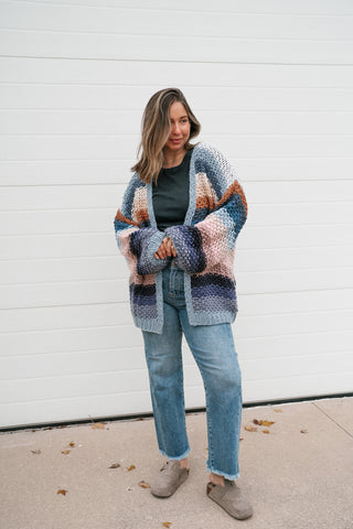 Model holding the open front of the chunky striped knit cardigan, showing the relaxed oversized fit and hip length