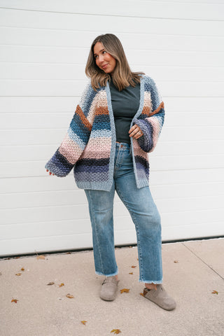 Model lifting her arms to show the full balloon sleeves and ribbed cuffs of the oversized striped knit cardigan
