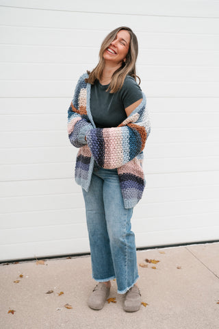 Smiling model wearing the multicolor striped crochet cardigan with a dark tee and cropped jeans
