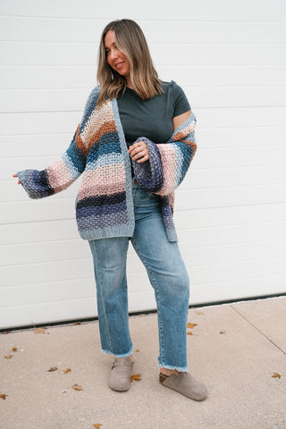 Model holding out one balloon sleeve to show the volume of the oversized striped crochet cardigan