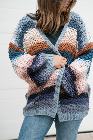 Close-up of the hand-crochet stitch texture and ribbed hem on the striped open cardigan in blue, blush, rust and navy