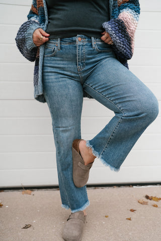 Model lifting one knee to show the stretch of the medium wash high rise ankle straight jeans