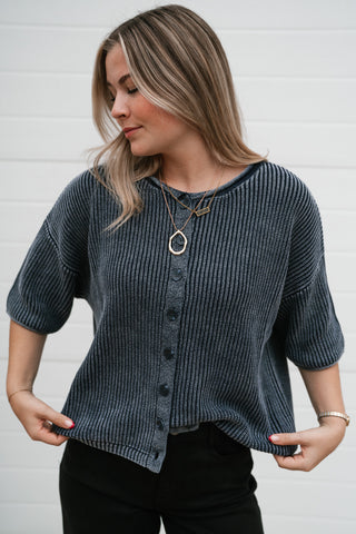 Model holding the hem of the navy short sleeve knit cardigan to show the waist-length fit