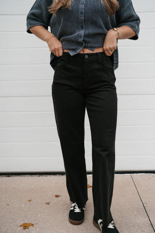 Front view of the black high rise wide leg jeans with front crease detail and frayed ankle hem
