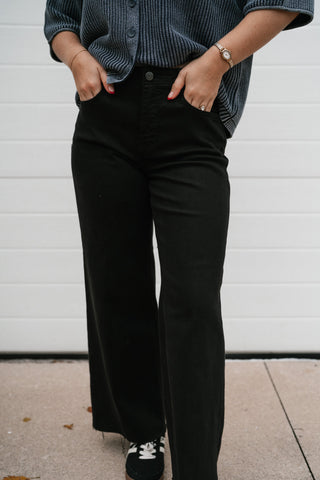 Close-up front view of the black high rise wide leg jeans with hands in pockets