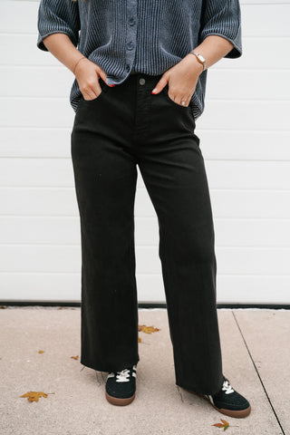 Front view of the Risen Parker black high rise wide leg jeans with raw hem and black sneakers