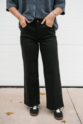 Model with hands in the front pockets of the black Risen wide leg ankle jeans